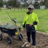 Woman in PPE wear with work equipment in field and horse in background