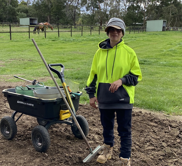 Woman in PPE wear with work equipment in field and horse in background