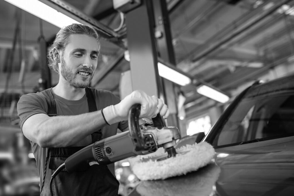 Polishing machine. Young adult smiling man polishing a car using special machine at service station